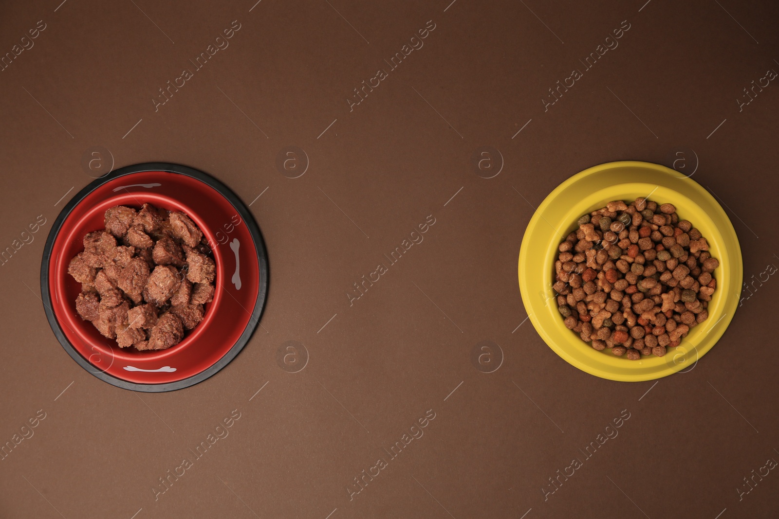 Photo of Dry and wet pet food in feeding bowls on brown background, flat lay. Space for text