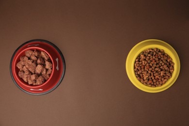 Dry and wet pet food in feeding bowls on brown background, flat lay. Space for text