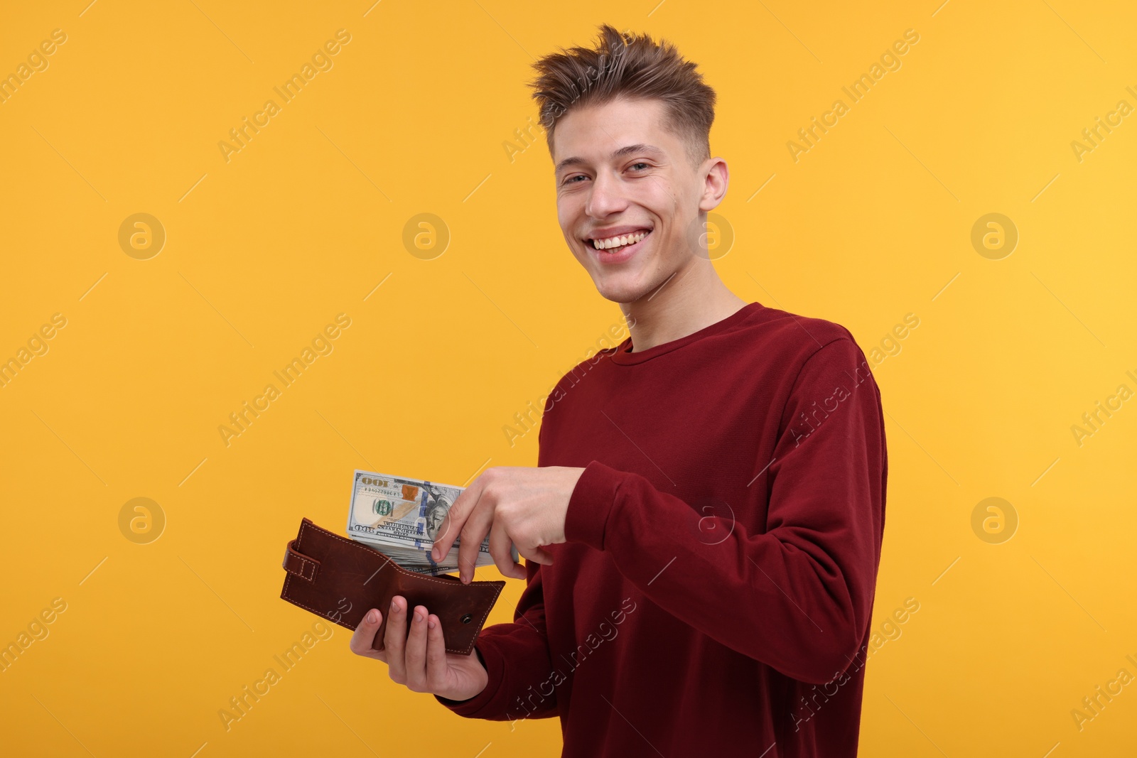 Photo of Happy man putting money into wallet on yellow background