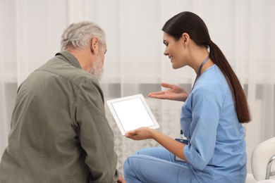 Photo of Smiling nurse with tablet talking to elderly patient in hospital