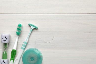 Photo of Tongue cleaner, dental floss, toothbrush and hourglass on white wooden table, flat lay. Space for text