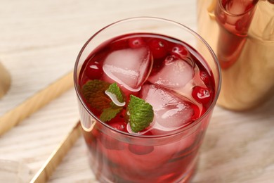 Tasty cranberry cocktail with ice cubes and mint in glass on light table, closeup