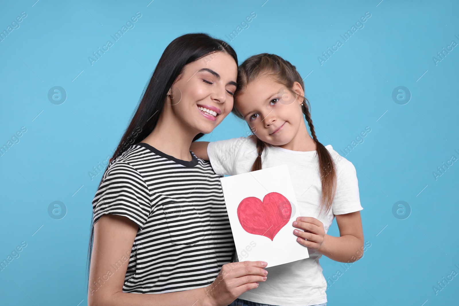 Photo of Happy woman with her cute daughter and handmade greeting card on light blue background. Mother's day celebration