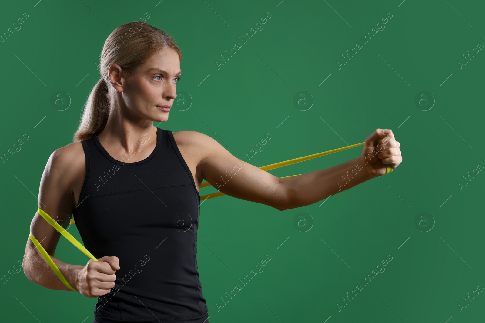 Photo of Athletic woman exercising with elastic resistance band on green background