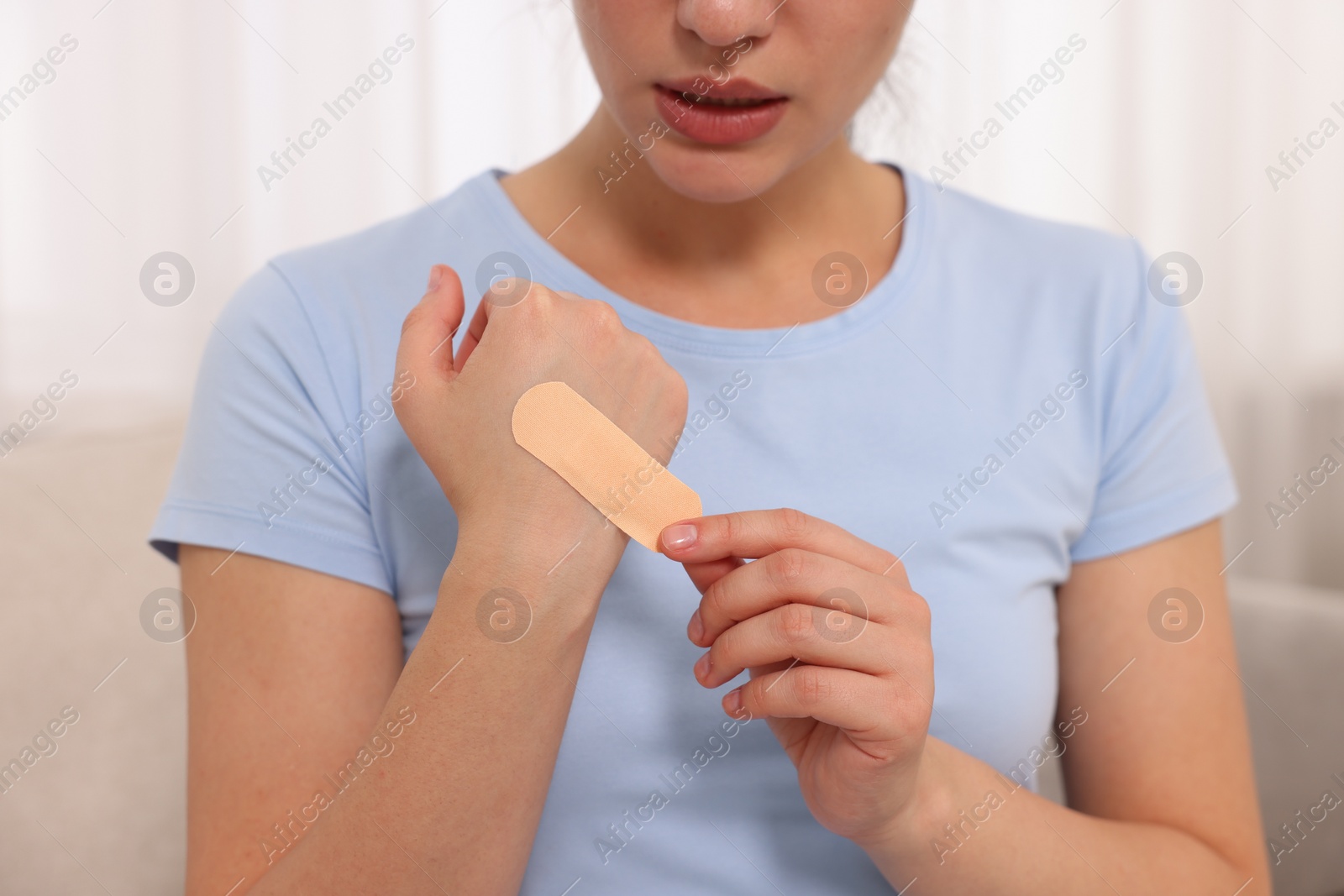 Photo of Woman putting sticking plaster onto hand indoors, closeup