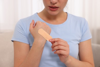 Woman putting sticking plaster onto hand indoors, closeup