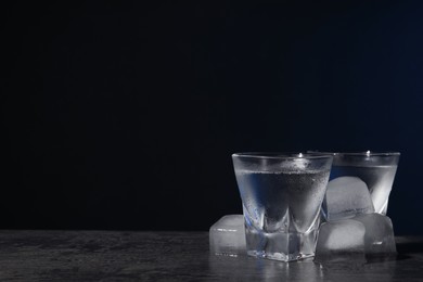 Photo of Vodka in shot glasses with ice on black table against dark background. Space for text