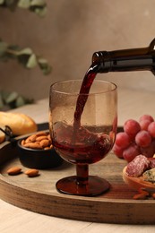 Photo of Pouring red wine into glass at wooden table, closeup