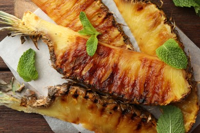 Photo of Tasty grilled pineapple pieces and mint leaves on wooden table, closeup