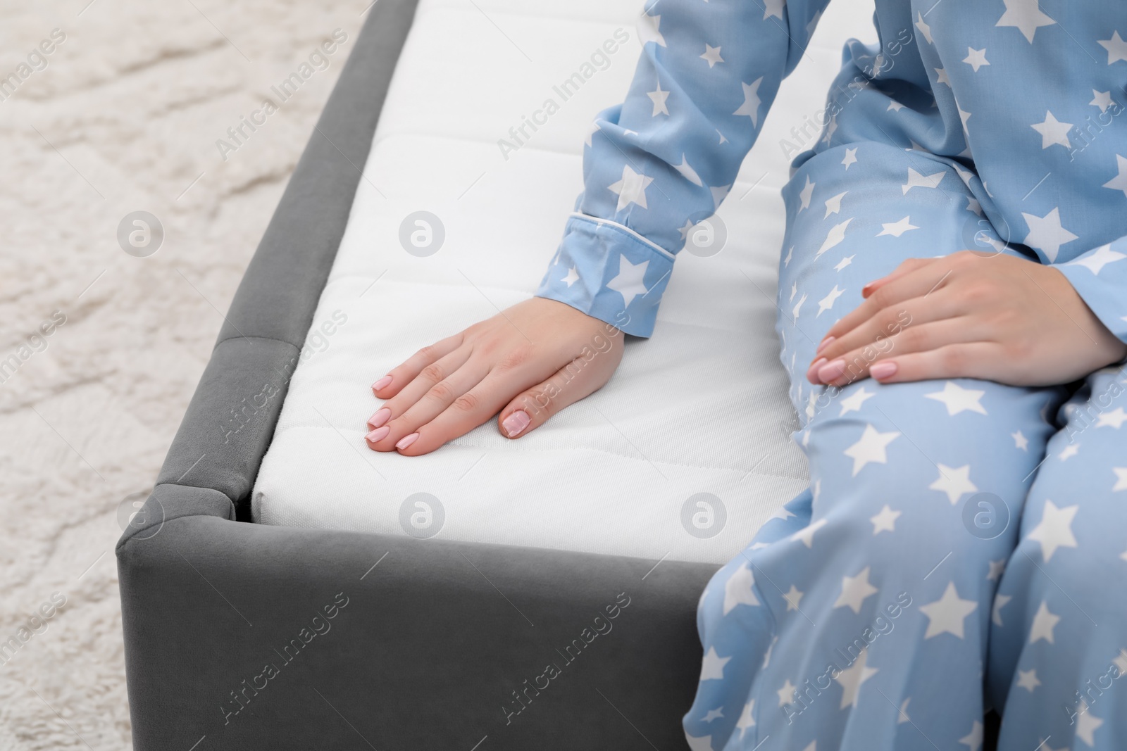 Photo of Woman sitting on new soft mattress indoors, closeup