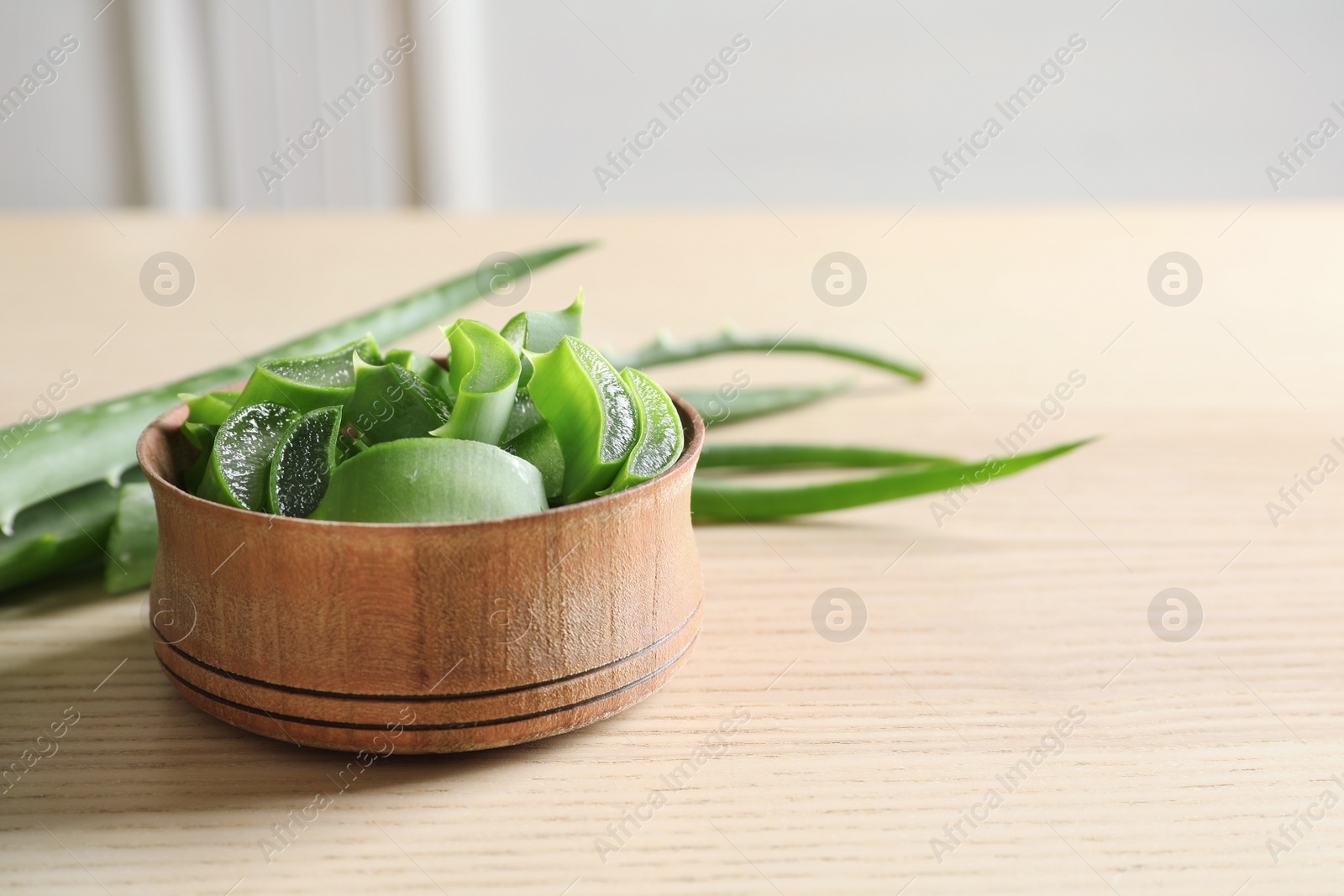 Photo of Bowl with sliced aloe vera leaves and space for text on wooden table