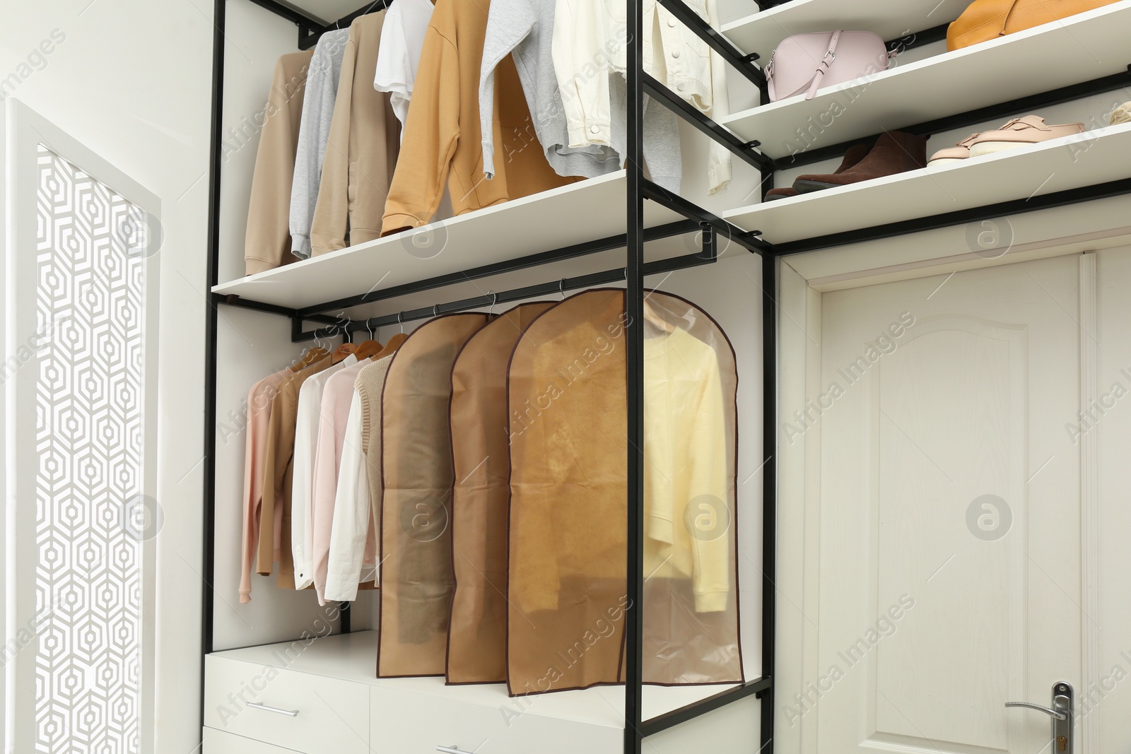 Photo of Garment bags with clothes on rack in dressing room