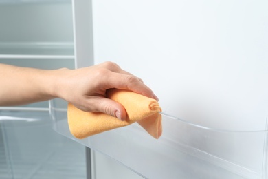 Woman cleaning empty refrigerator with rag, closeup