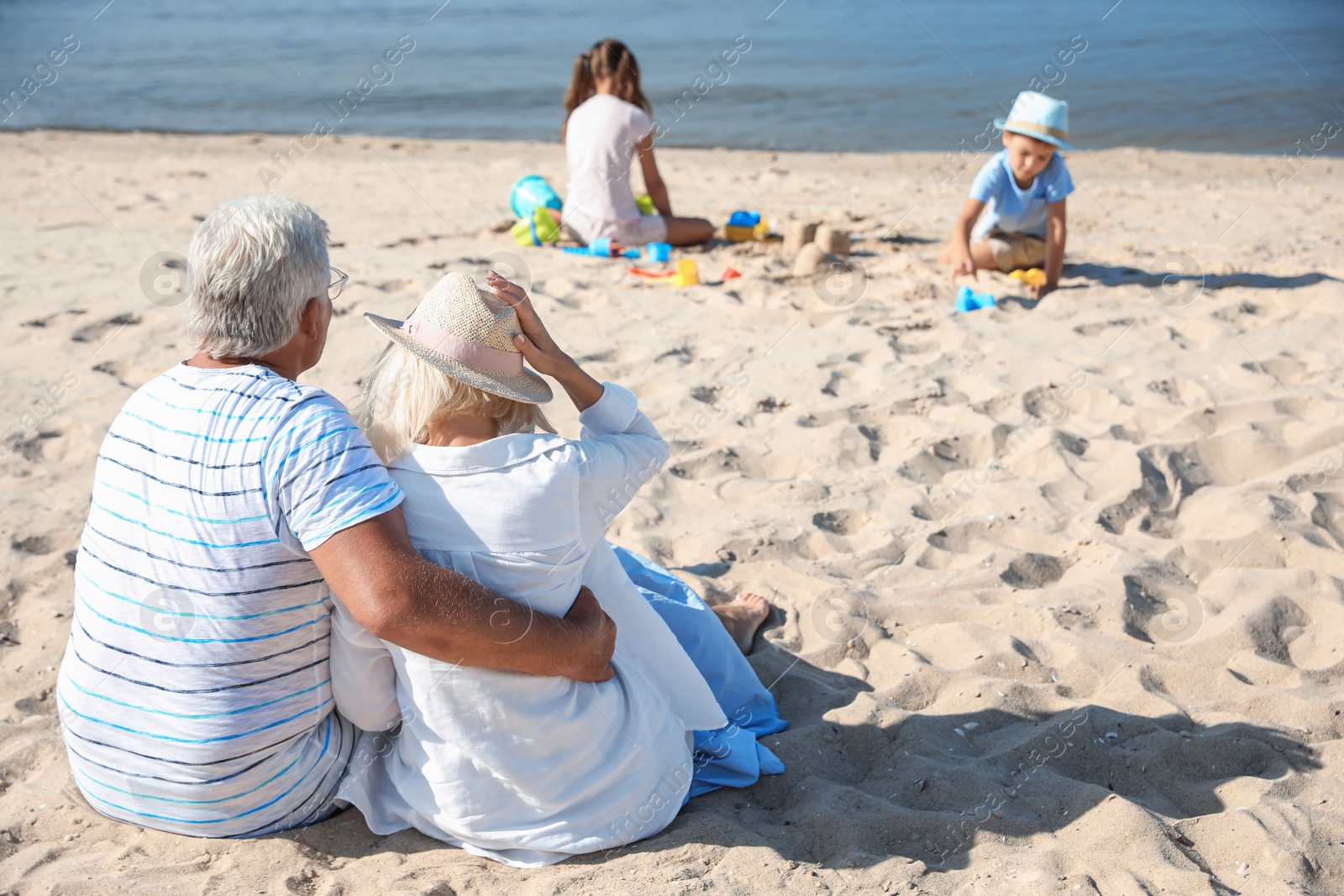 Photo of Little children playing on sea beach, focus on grandparents