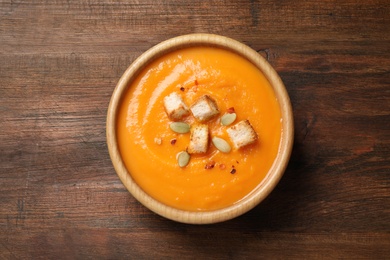 Bowl with tasty pumpkin cream soup on wooden table, top view