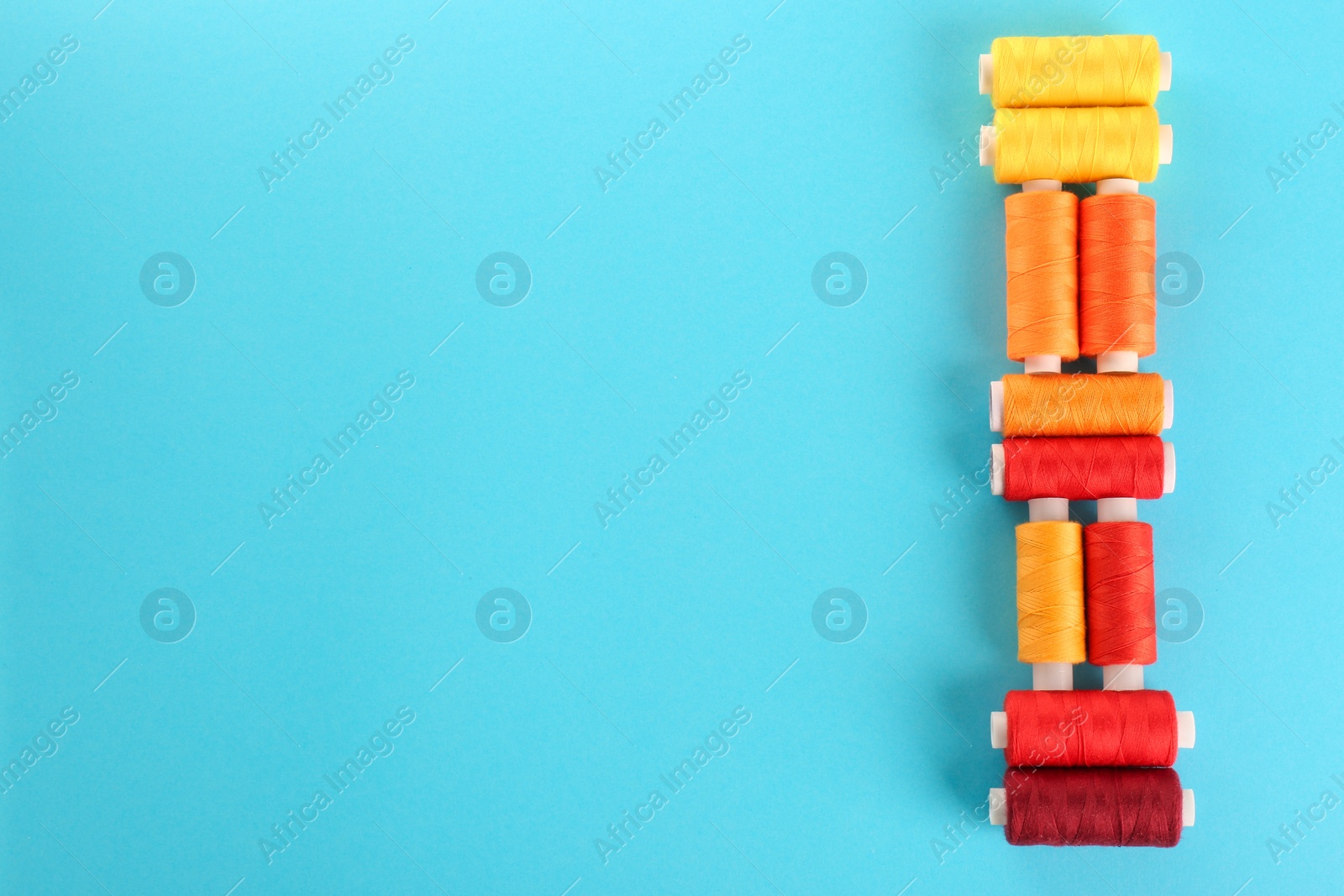 Photo of Different colorful sewing threads on light blue background, flat lay. Space for text