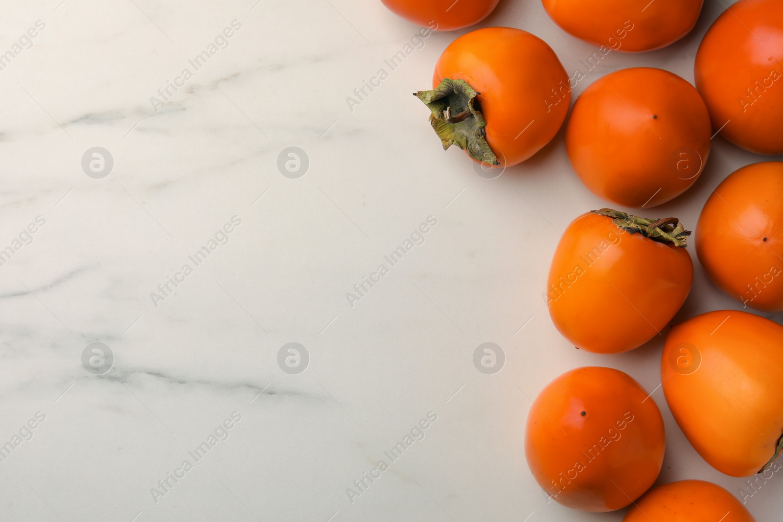 Photo of Delicious ripe persimmons on white marble table, flat lay. Space for text