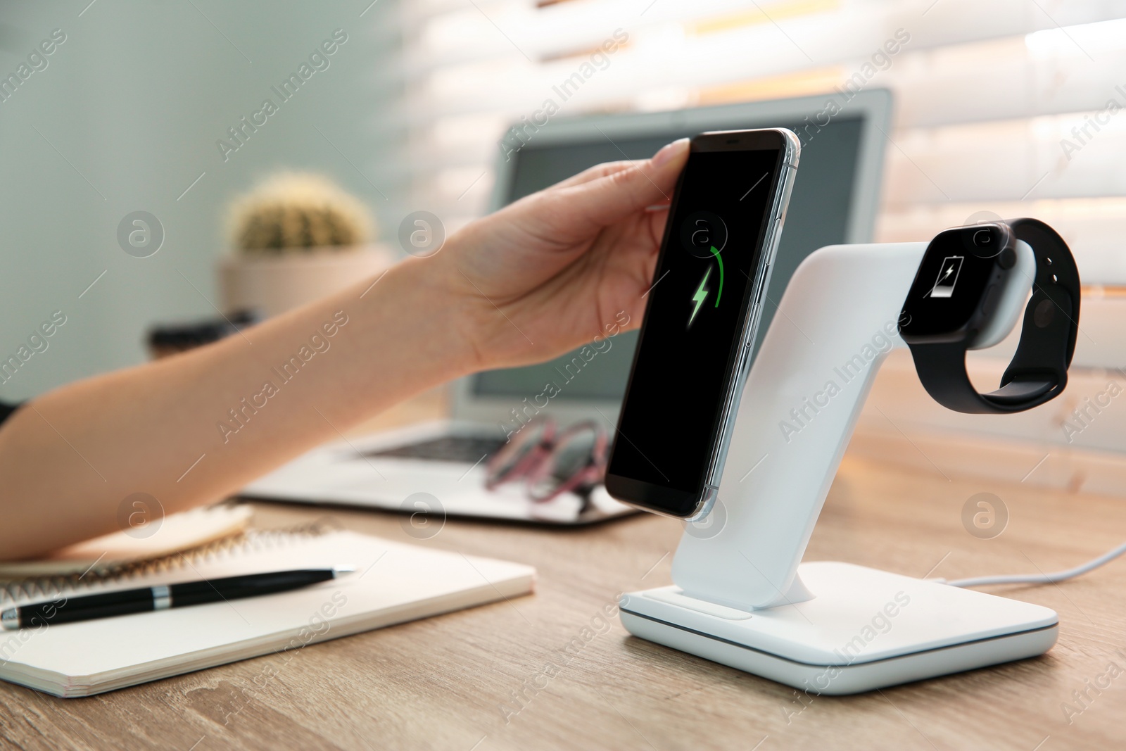 Photo of Woman putting mobile phone onto wireless charger at wooden table, closeup. Modern workplace accessory