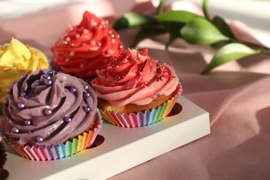 Photo of Delicious cupcake with bright cream on pink fabric, closeup