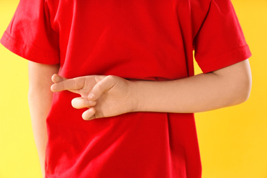 Photo of Little boy with crossed fingers on yellow background, closeup. April fool's day