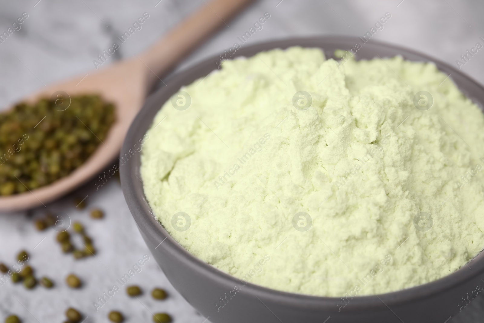 Photo of Mung bean flour in bowl and seeds on white textured table, closeup