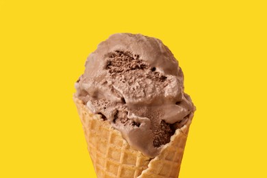 Photo of Delicious chocolate ice cream in waffle cone on yellow background, closeup