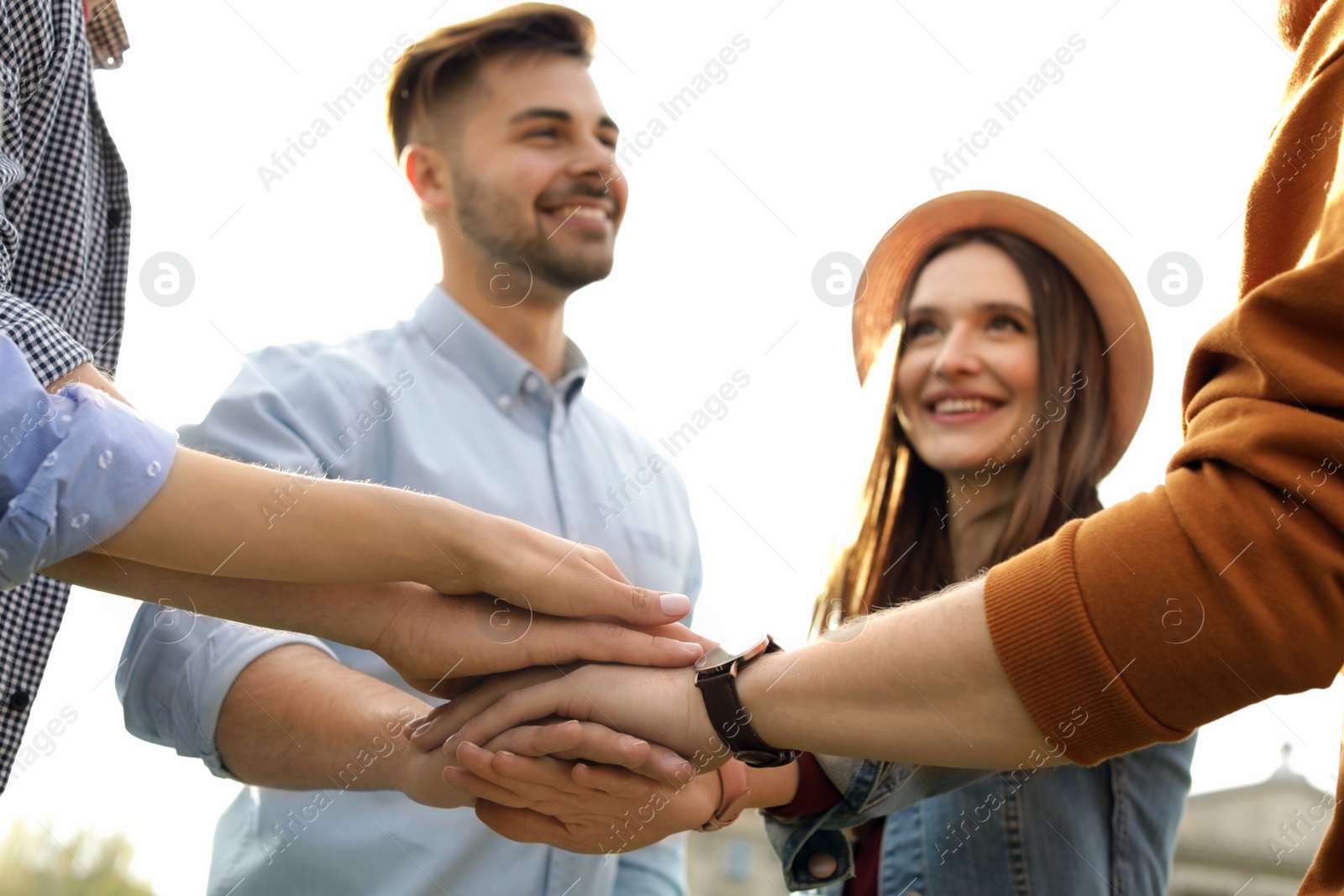 Photo of Happy young people holding hands together outdoors on sunny day, closeup