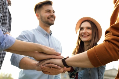 Happy young people holding hands together outdoors on sunny day, closeup