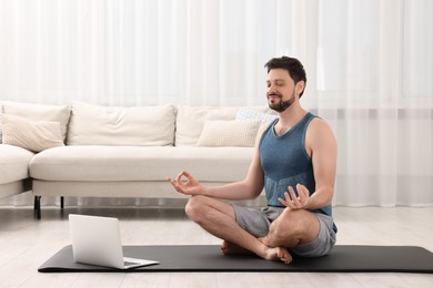 Photo of Man in sportswear meditating near laptop at home. Harmony and zen