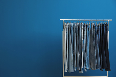 Photo of Rack with stylish jeans on blue background. Space for text