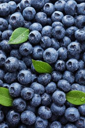 Wet fresh blueberries with green leaves as background, top view