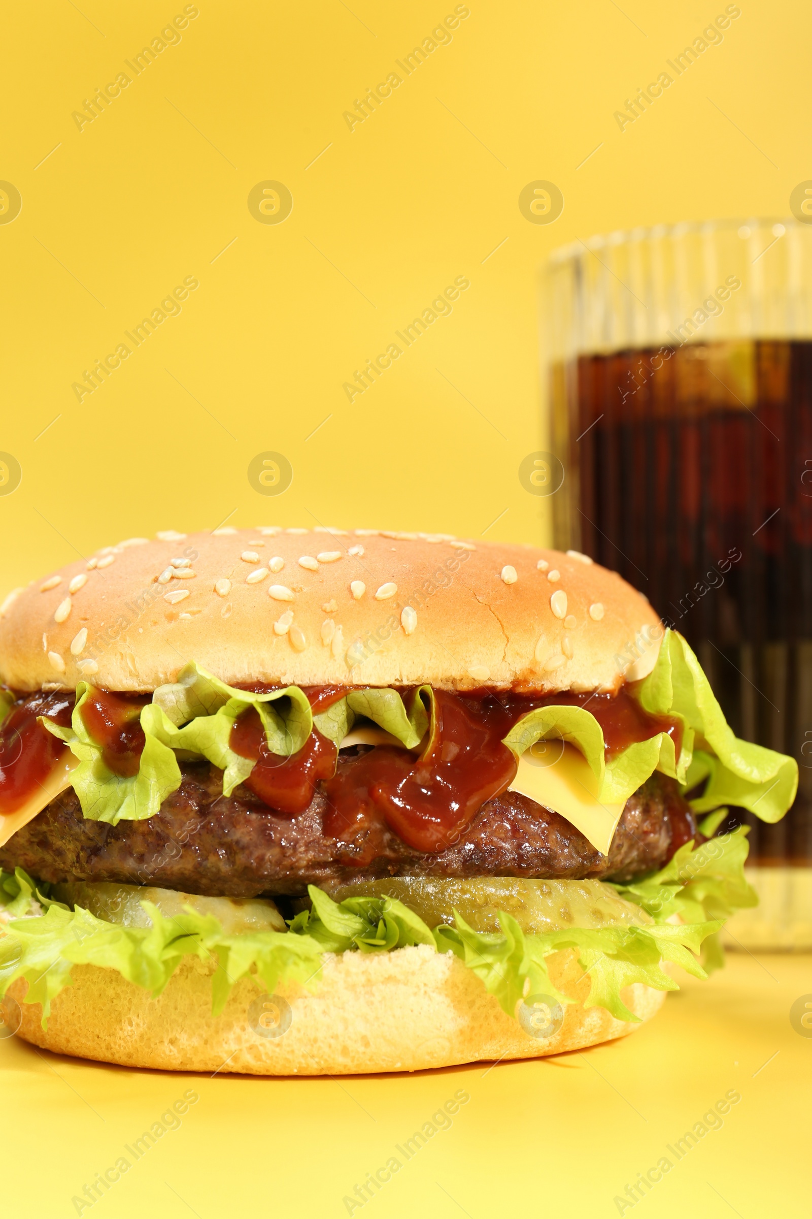 Photo of Burger with delicious patty and soda drink on yellow background, closeup