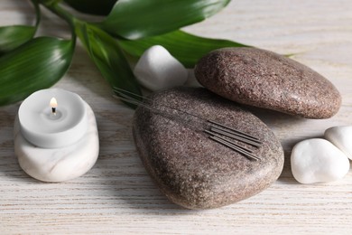 Photo of Stones with acupuncture needles and burning candle on white wooden table