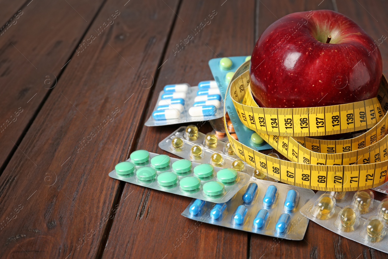 Photo of Weight loss pills and apple with measuring tape on wooden background. Space for text