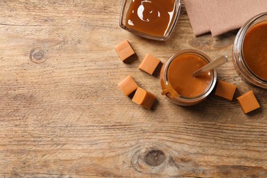 Tasty salted caramel and candies on wooden table, flat lay. Space for text