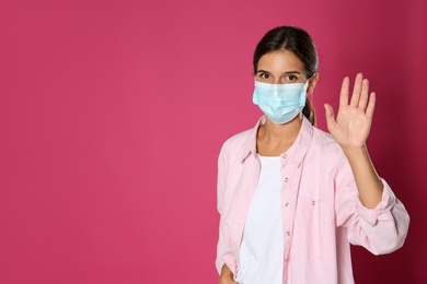 Photo of Woman in protective mask showing hello gesture on pink background, space for text. Keeping social distance during coronavirus pandemic