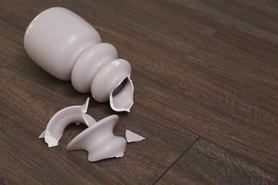 Photo of Broken pink ceramic vase on wooden floor. Space for text