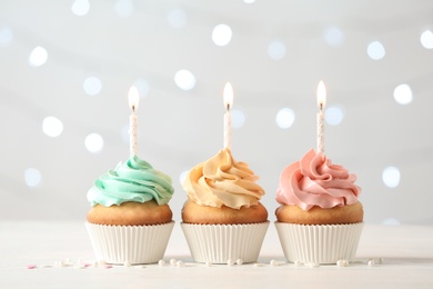 Photo of Delicious birthday cupcakes with burning candles on blurred lights background