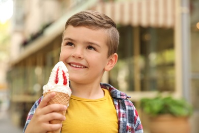 Cute little boy with delicious ice cream outdoors, space for text