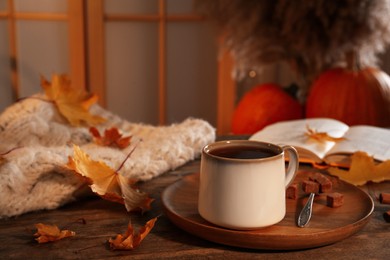 Photo of Cup of aromatic tea, sweater, book and autumn leaves on wooden table indoors, space for text