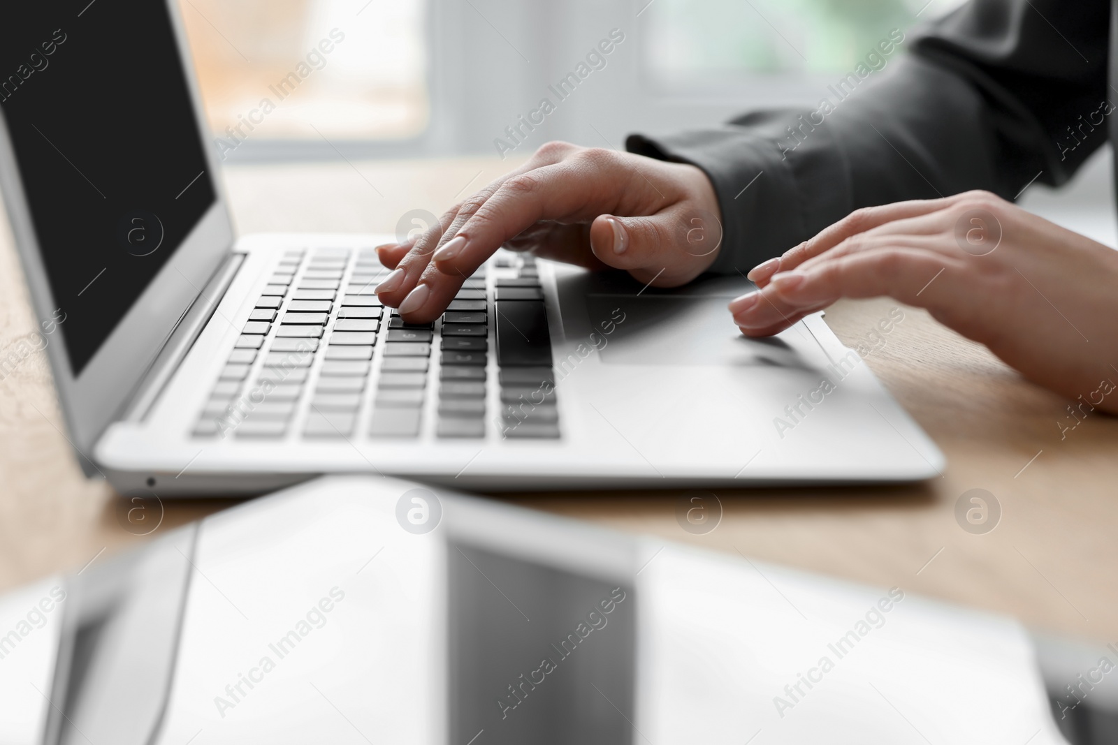 Photo of Woman with tablet working on laptop at wooden table, closeup. Electronic document management