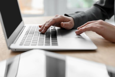 Photo of Woman with tablet working on laptop at wooden table, closeup. Electronic document management