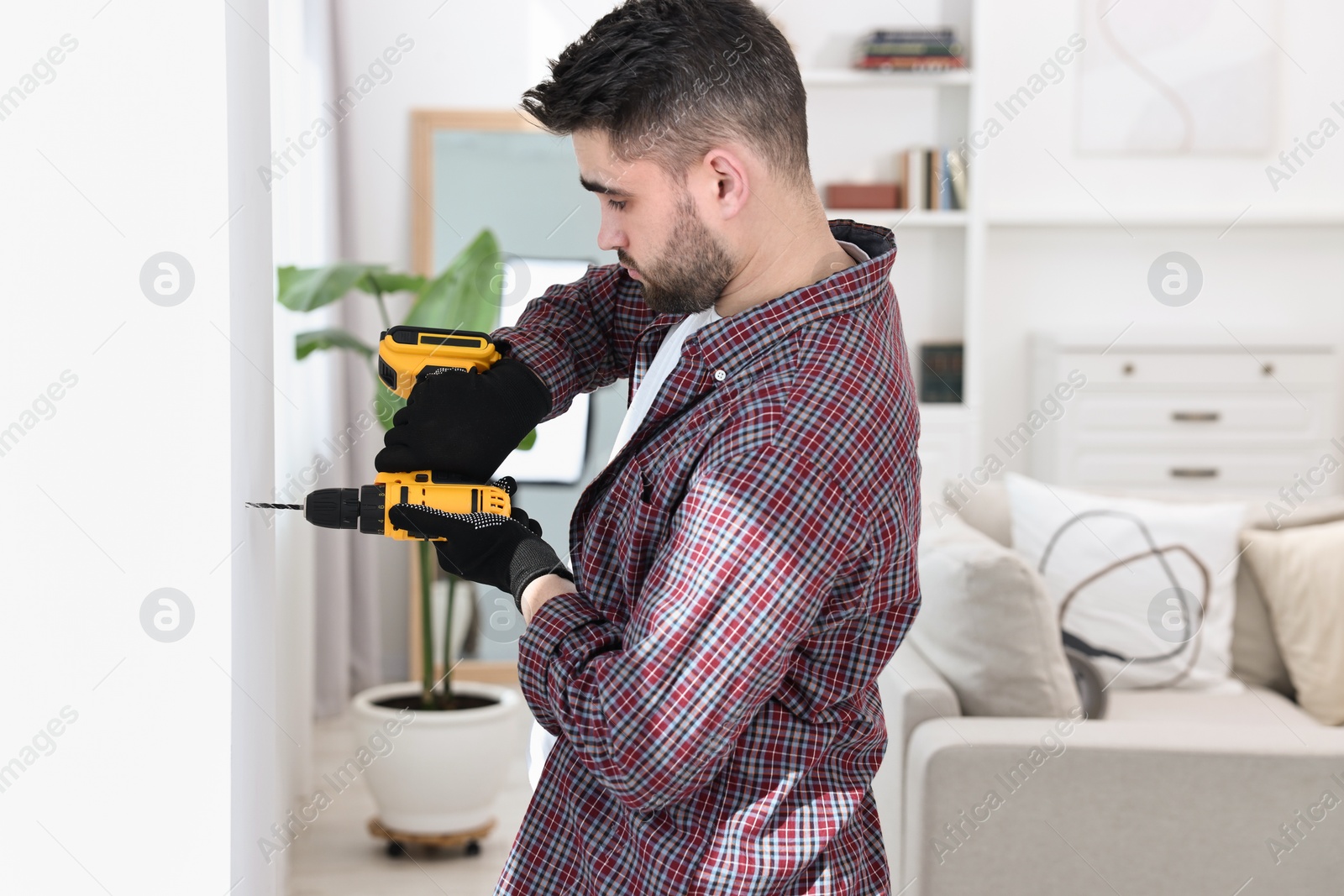 Photo of Young handyman working with electric drill at home