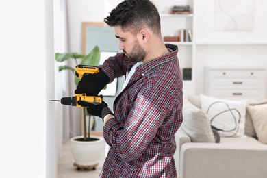 Photo of Young handyman working with electric drill at home