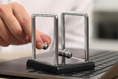 Photo of Man playing with Newton's cradle and laptop on table, closeup. Physics law of energy conservation