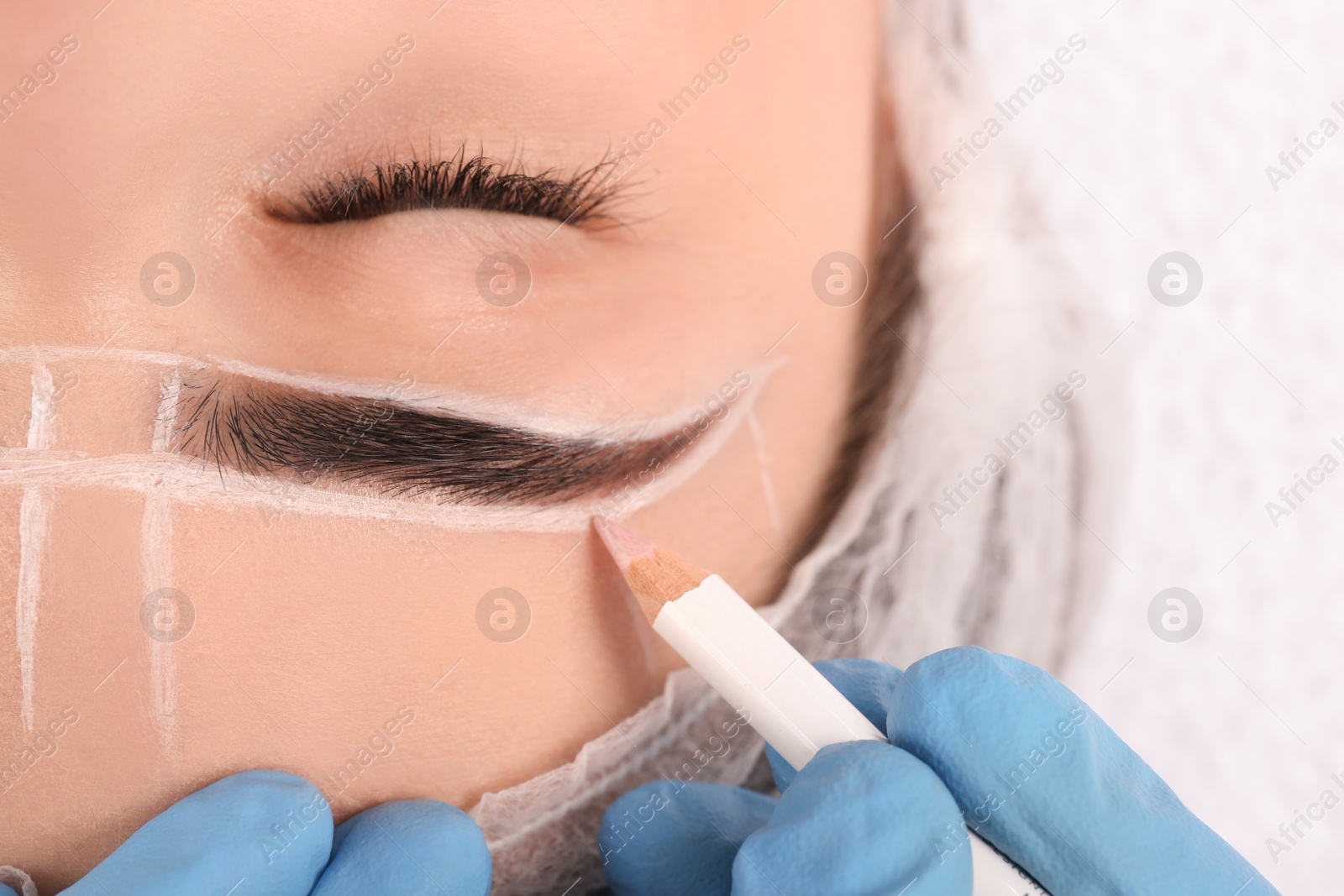 Photo of Cosmetologist preparing young woman for eyebrow permanent makeup procedure, closeup