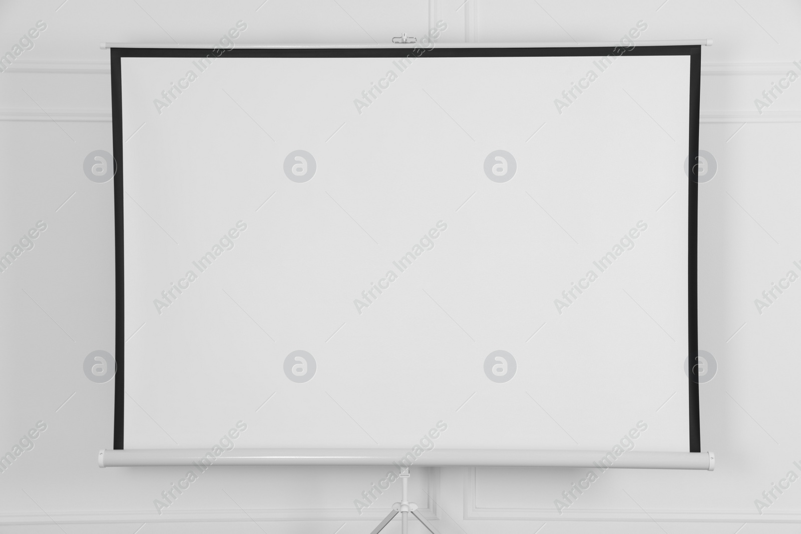 Photo of Blank projection screen near white wall indoors. Space for design