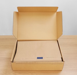 Photo of Open cardboard box with item wrapped in kraft paper on wooden table. Delivery service