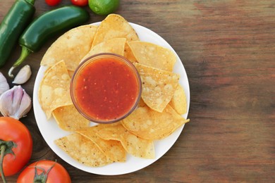 Tasty salsa sauce with tortilla chips and ingredients on wooden table, flat lay. Space for text