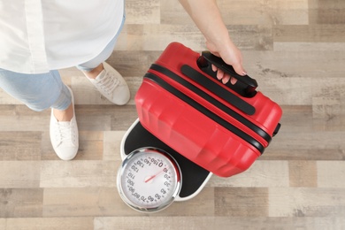 Woman weighing modern suitcase indoors, top view